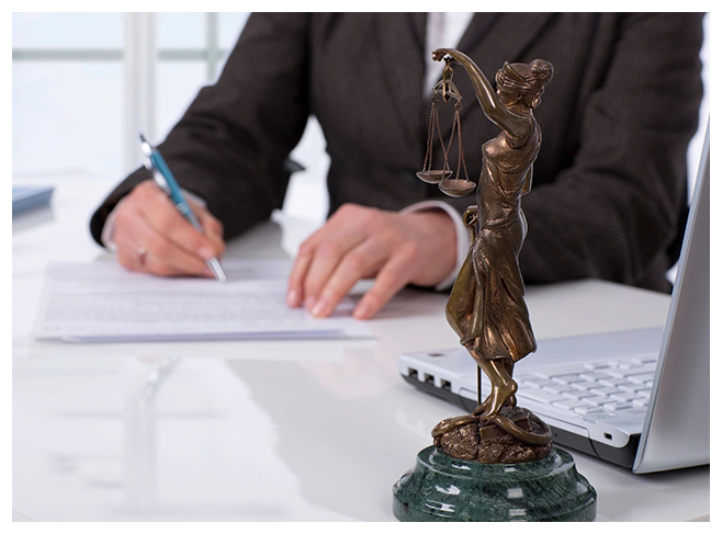 A person writing on paper near a statue of lady justice.