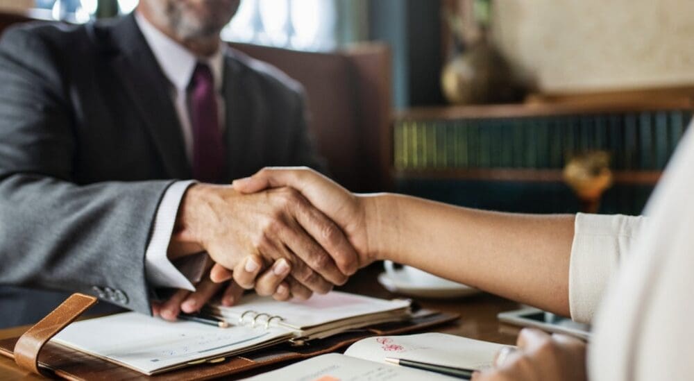 A man and woman shaking hands over paperwork.