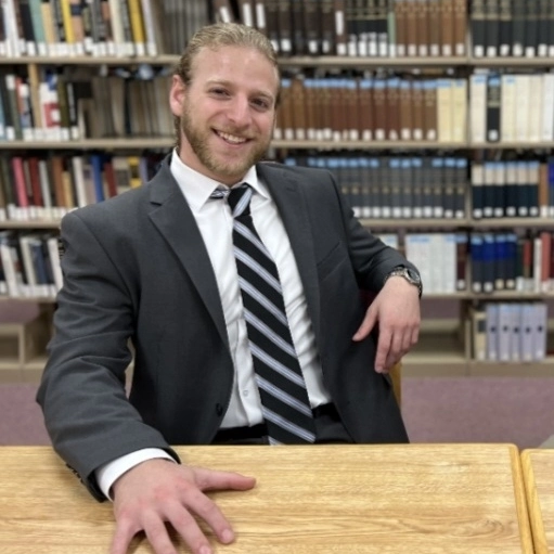 Man in suit sitting at a desk in a library.