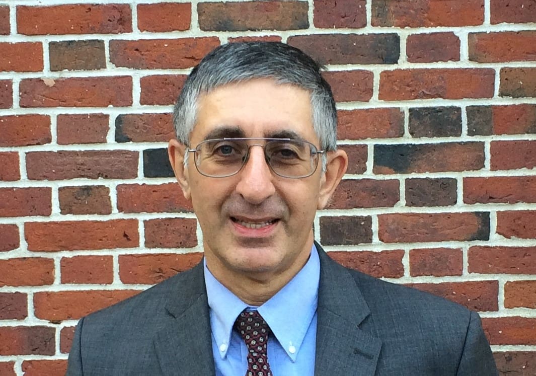 Man in suit smiling against brick wall.