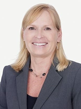 Smiling woman in gray blazer with necklace.