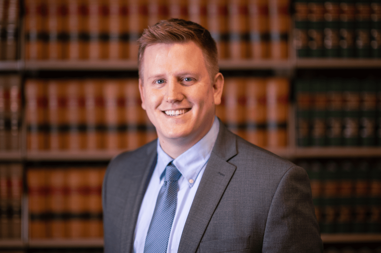 Smiling man in suit against bookshelf.