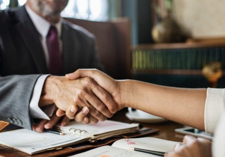 A man and woman shaking hands over paperwork.